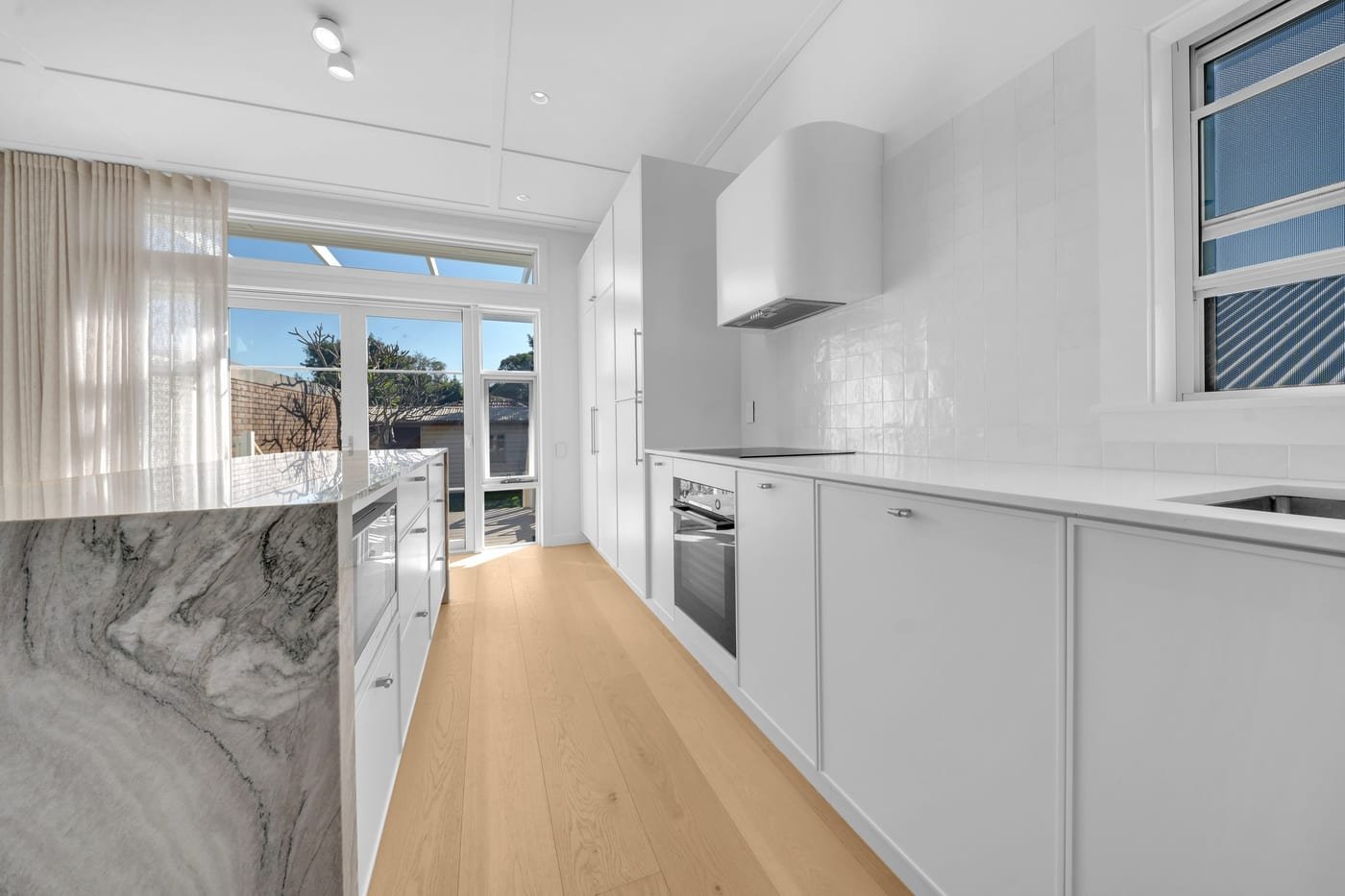 Kitchen renovations Sydney: bright white kitchen with warm timber floors and a stone island by NK Kitchens & Joinery